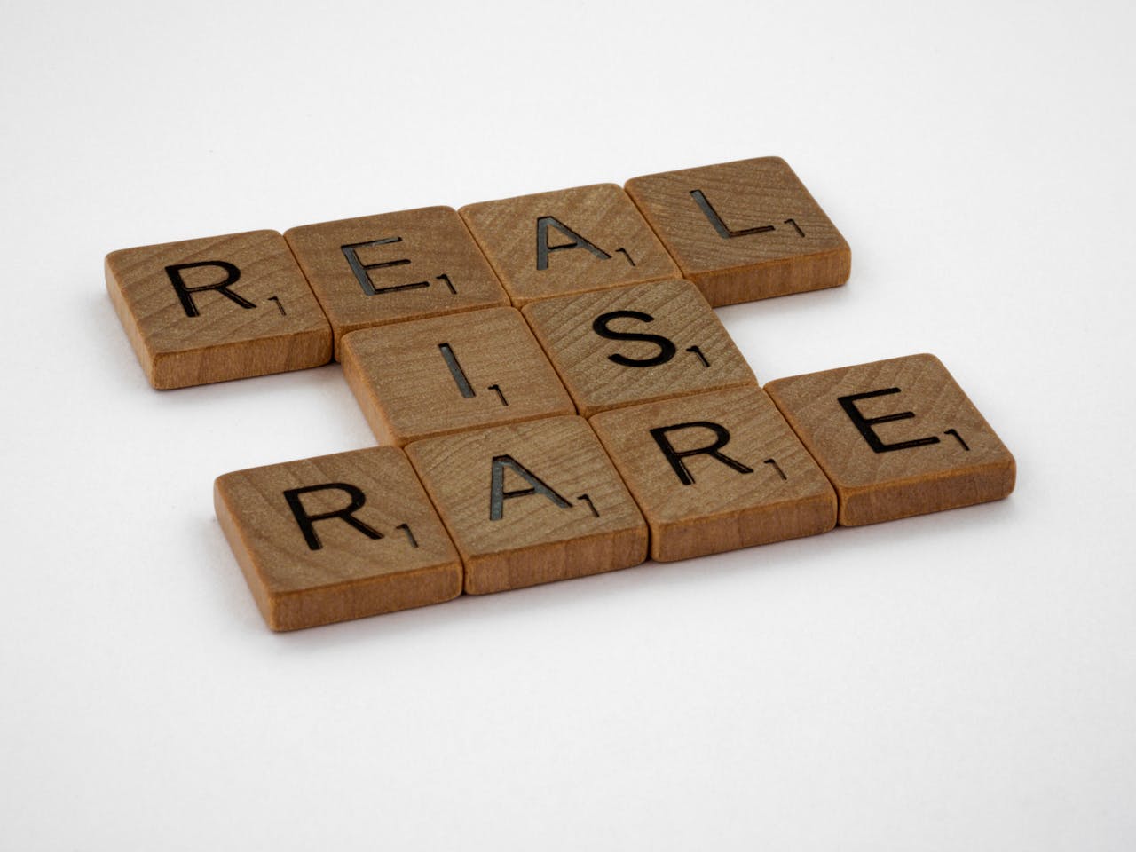 Wooden Scrabble tiles arranged to spell 'Real is Rare' on a white background.
