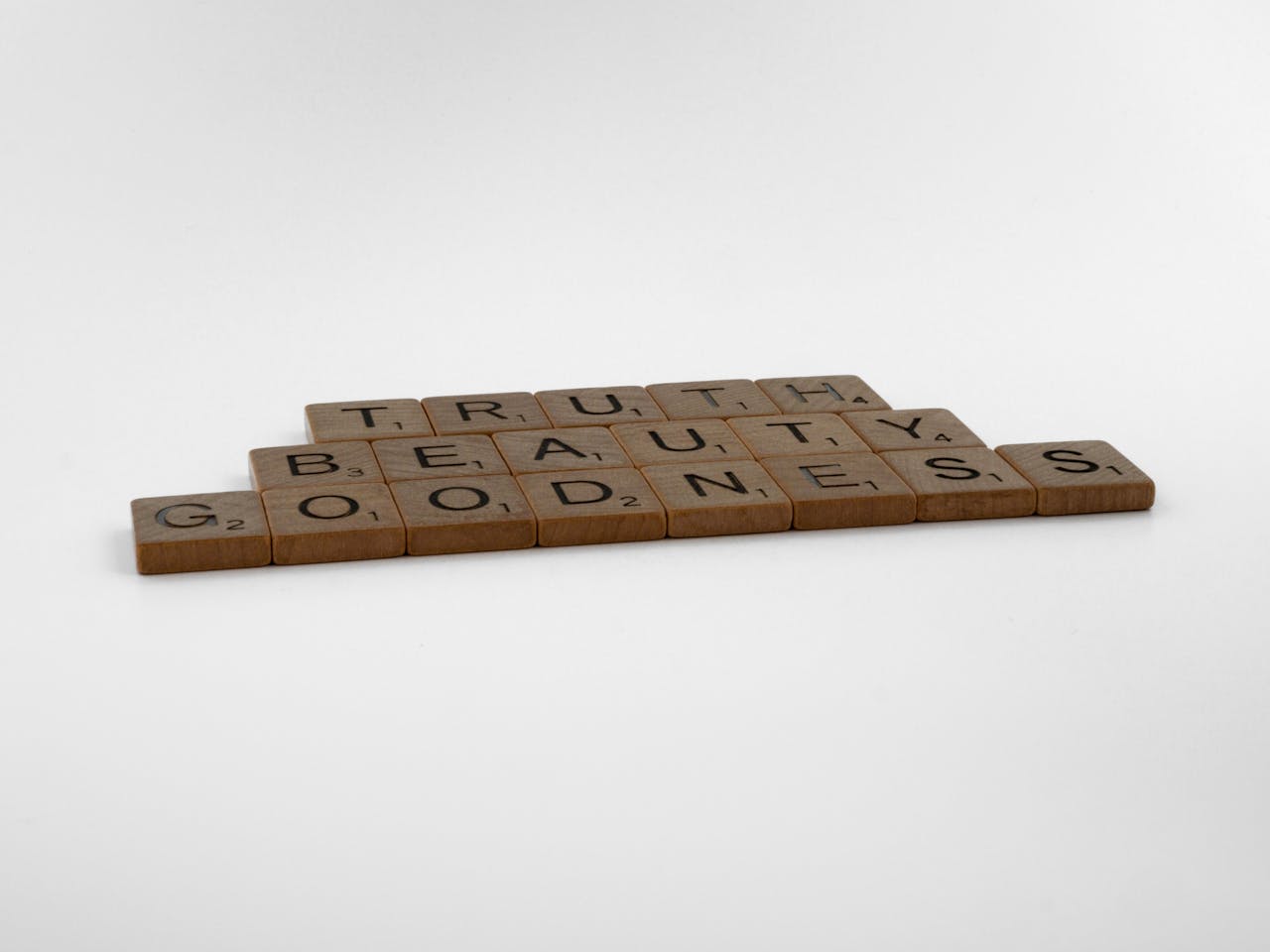 Wooden Scrabble tiles forming the words Truth, Beauty, and Goodness on a white background.