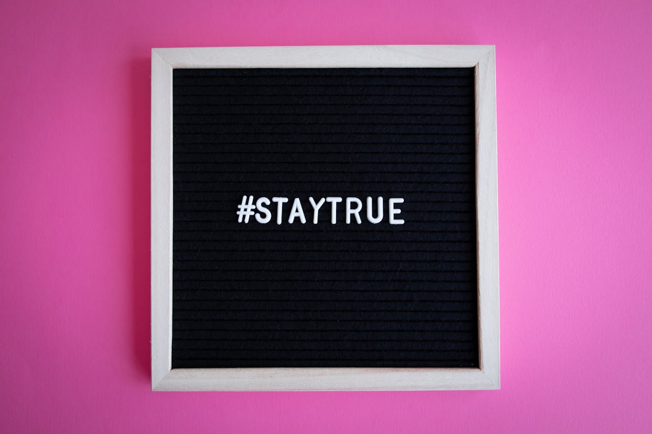 Black letter board with motivational text '#StayTrue' on pink background.